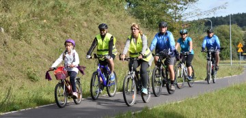 Grupa rowerzystów z dzieckiem na czele na asfaltowej ścieżce rowerowej